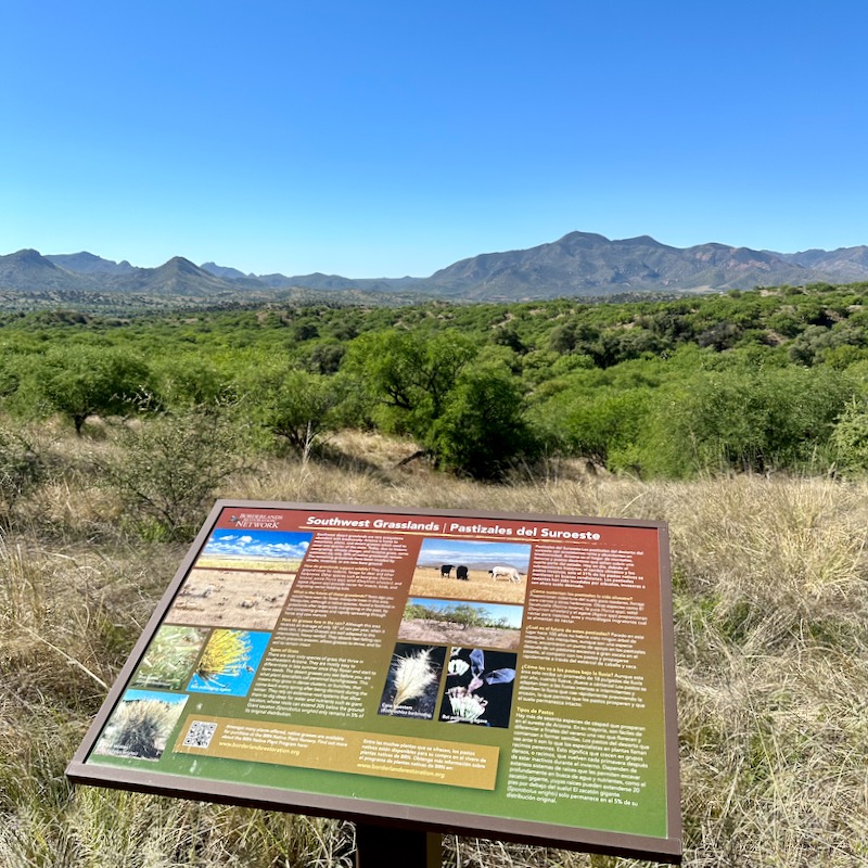 Borderlands Wildlife Preserve signboard along the trail with mesquite trees and mountains in the background