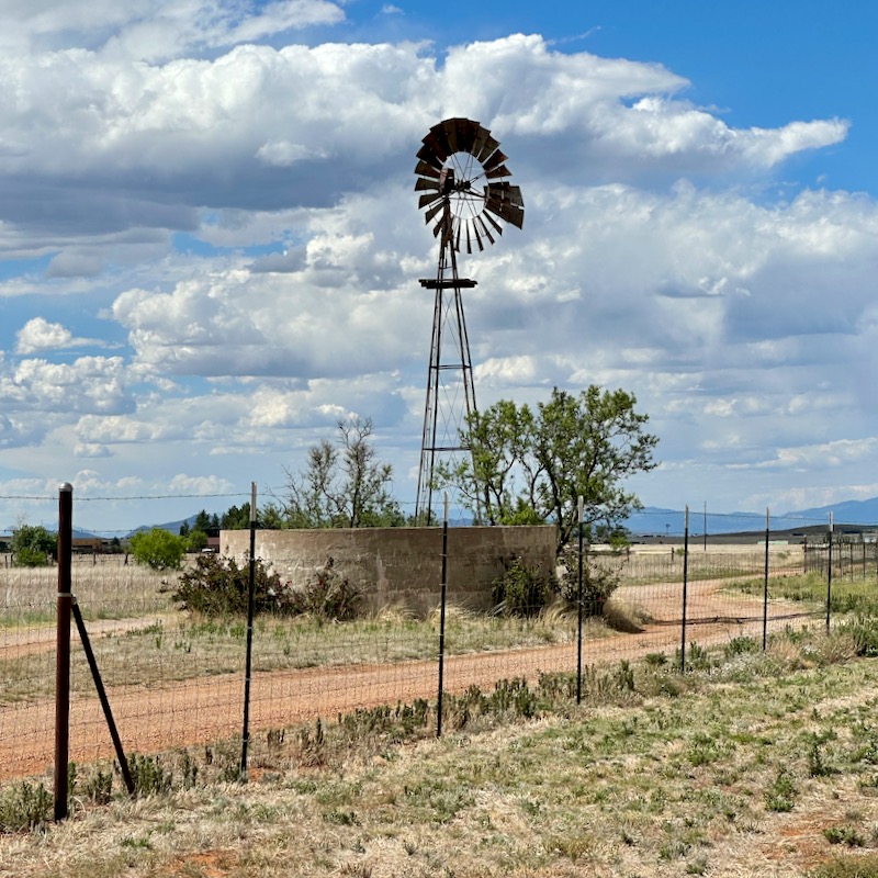 Photo of windmill and water tank behind fence with clouds in the sky