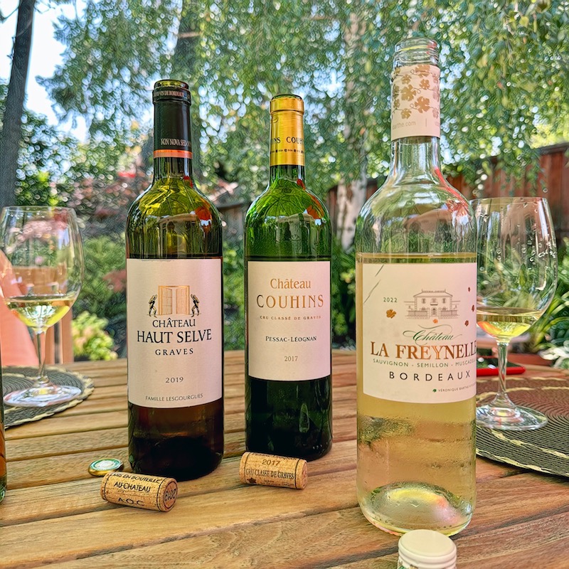 Photo of three white Bordeaux wines on a table in the garden